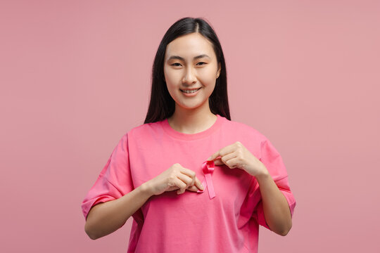 Young woman pinning pink ribbon on shirt, supporting breast cancer awareness - Powered by Adobe