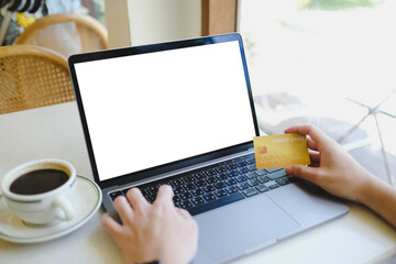 A person holding a credit card while using a laptop with a blank white screen, perfect for e-commerce or online payment mockups.