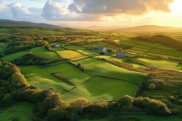Aerial view of lush green patchwork fields and farmland under a golden sunset sky with scattered clouds and distant hills