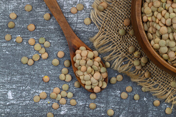 Pile lentil in wooden spoon isolated on wooden background. Top view.