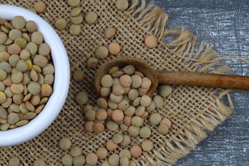 Pile lentil in wooden spoon isolated on wooden background. Top view.