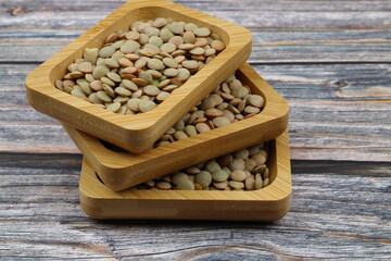 Green lentils in wooden bowl on wooden table background. Top view, copy space. Flat lay.