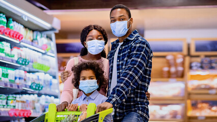 Portrait of young black family with little child wearing face masks while shopping for groceries at...