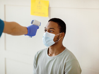 Young black man having his temperature measured by infrared thermometer at clinic before getting...