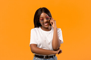 Cute attractive black woman looking down and smiling, wearing stylish sunglasses, closeup portrait,...