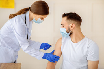 Vaccination against covid-19. Female doctor in face mask injecting coronavirus vaccine to male...