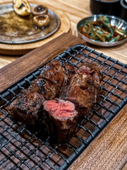 Close-up of juicy grilled beef cubes with a pink center, served on a wooden board with a metal grate, highlighting the texture and sear marks.