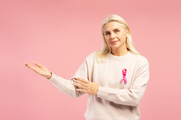 Woman showing pink ribbon for breast cancer awareness on pink background
