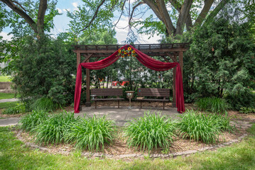 Romantic outdoor pergola decorated with burgundy drapes and floral arrangement 