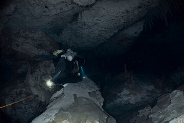 Diver explores a dark, mysterious cave system with a powerful light.