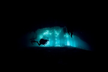 Diver explores a dark, mysterious underwater cave illuminated by a single light.