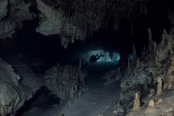 A diver explores a dark, expansive cave system with stunning stalactites.
