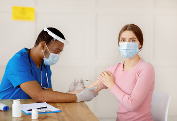 Fototapeta premium Antiviral protection and immunization. Doctor vaccinating female patient against coronavirus, injecting covid-19 vaccine at hospital. Medical protection against viral diseases concept