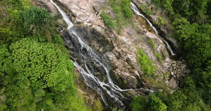 Rocky waterfall surrounded by vibrant green jungle and tropical vegetation. Na Mueang Waterfall. Ko Samui, Thailand.
