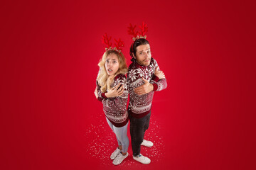 Full length portrait of young couple in Christmas sweaters shivering on red background, above view