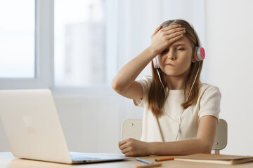 Young girl with headphones showing frustration while studying at a desk, representing challenges in...