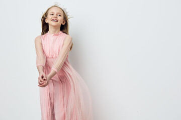 Cheerful young girl in a flowing pink dress smiles joyfully against a minimalist light background,...