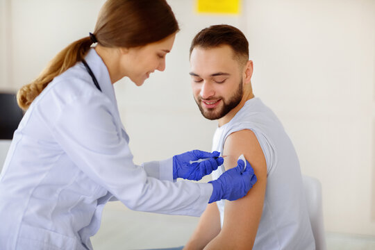 General practitioner vaccinating young male patient, making covid-19 vaccine injection at clinic. Happy millennial guy receiving protection against coronavirus, participating in immunization campaign