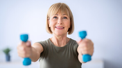 Sports during quarantine. Attractive senior woman doing fitness with dumbbells at home, exercising...