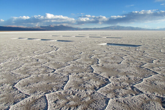 Salt flat lake in South America. Salt piles on Salar, salt production. Salt lake plato, flat plaine covered with white salt, blue water, mountains on horizon. Uyuni Salar, Bolivia, Altiplano landscape