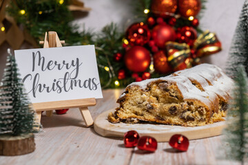Note with saying MERRY CHRISTMAS congratulations. Traditional German Christmas stollen cake in...