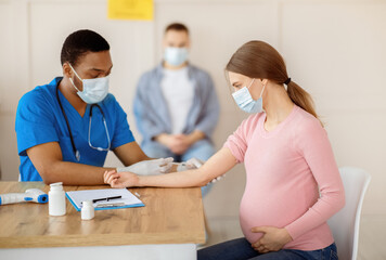 African American doctor giving Covid-19 vaccine injection to young pregnant woman at health centre....