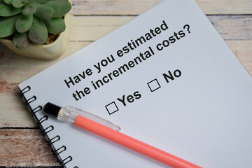 Have you estimated the incremental costs write on book isolated on Wooden Table. A person is...