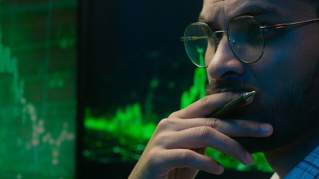 Indian Arabian man programmer coder hacker male guy trader IT specialist thoughtful analyst thinking analysing cryptocurrency financial chart graph solve ponder hesitate broker looking monitor indoor