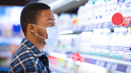 Side view of black guy in disposable mask selecting dairy products at mall during covid-19...