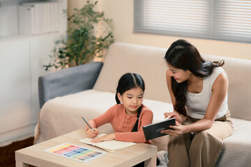 Mother helping her daughter with homework and using a digital tablet in living room