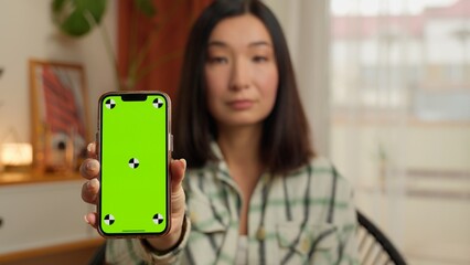 Serious Korean Japanese woman business businesswoman showing mobile phone green screen at camera...