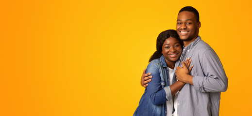 Fototapeta premium Portrait Of Affectionate Cheerful African American Couple Embracing While Posing Over Yellow Background, Happy Romantic Black Young Man And Woman Hugging And Smiling At Camera, Copy Space