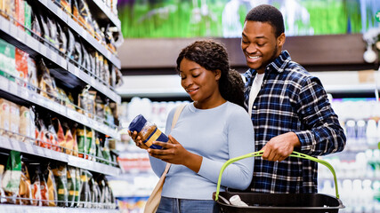 Young African American couple buying groceries, choosing good coffee at supermarket. Cheerful black...