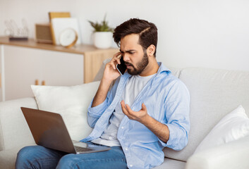Computer Problems. Frustrated arab freelancer guy talking on cellphone and looking on laptop screen...