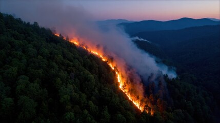 Fototapeta premium Wildfire erupts in forested mountains aerial view nature photography dusk environment environmental impact
