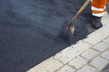 Man in a reflective vest is shoveling black gravel into a pothole