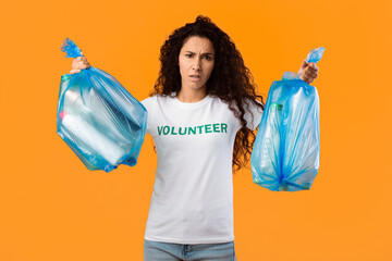 Displeased Female Volunteer Holding Two Plastic Garbage Bags Full Of Litter And Wasted Bottles...