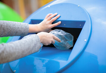 Waste Sorting Concept. Hand throwing single use plastic bag into blue recycle bin outdoors, unrecognizable lady caring about environment pollution level, cropped image, closeup