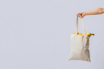 Hand Holding Blank Eco Tote Bag With Organic Fruits And Vegetables Over Light Studio Background,...