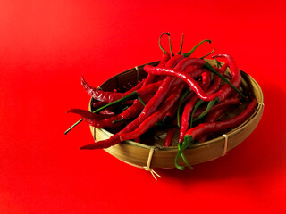Red chili peppers are arranged in a woven bamboo basket on red background