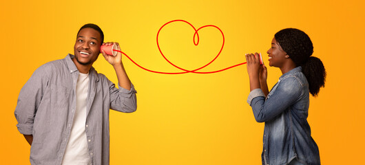 Love Message. Happy black woman whispering romantic words to her boyfriend via tin phone, standing...