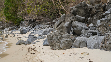 A secluded beach on a tropical island. A pile of boulders along the shore. Foam of waves on the sand. Green vegetation. Philippines. Palawan. El Nido. Ipil Beach