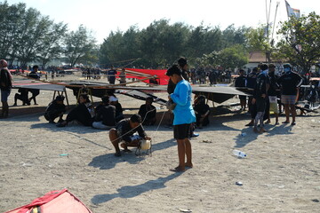 Indonesian boys sitting in the shade of a large kite on the beach