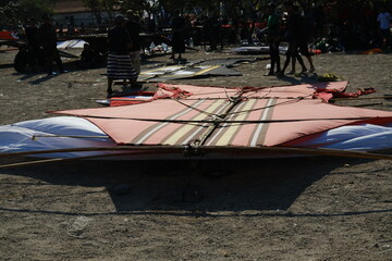 Large kite lying on sand surrounded by Indonesians