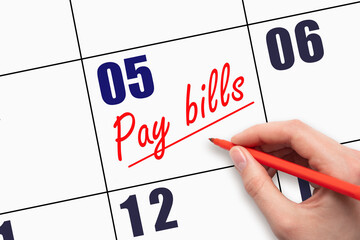 5th day of the month.  Hand writing Pay bills reminder and drawing a line on calendar with red pen...