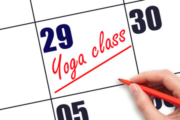29th day of the month.  Hand writing Yoga class reminder and drawing a line on calendar with red pen on white background. Concept of sport and fitness activity.  Planning and scheduling