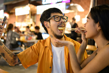 Young couple taking selfie while eating asian food in night market
