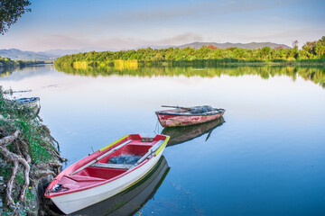 Obraz premium A red boat on river with a beautiful calming reflection of both boat itself and the surrounding Forest trees. , Scenic River Cruise on a Traditional small wooden Fishing with Ropes and Calm Views. 