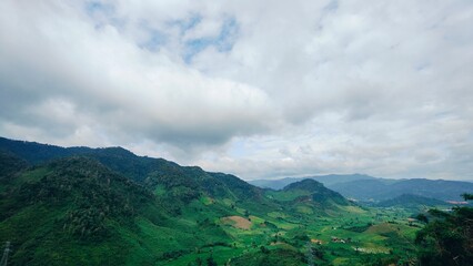 Green mountain and valley landscape in rural Laos with cloudy sky.  The dramatic sky above is...