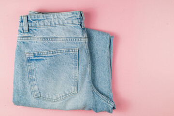 Casual light blue jeans folded on a pink background